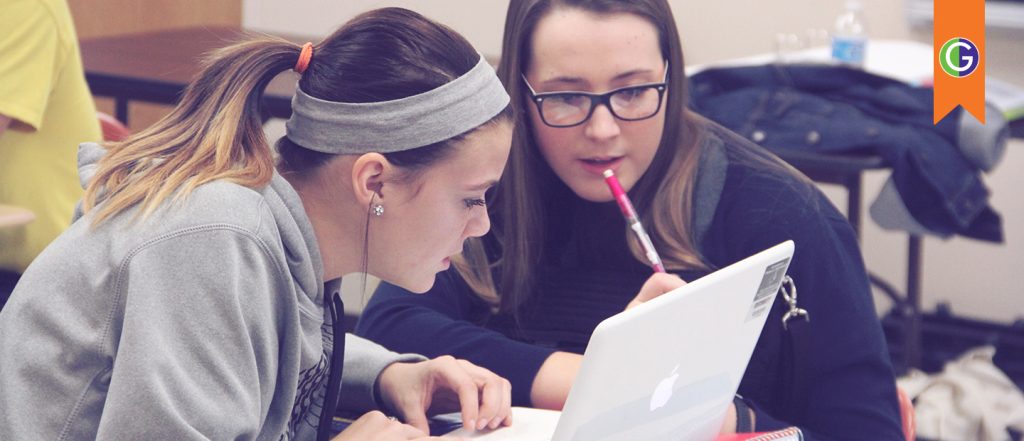 Graphic features a photo of two high school students in a classroom, seated closely and focused on a white laptop, and at the top right, an orange ribbon features the GEAR UP green and purple logo. The two female students in the photo are discussing their college application essays and preparing to start their college journey.